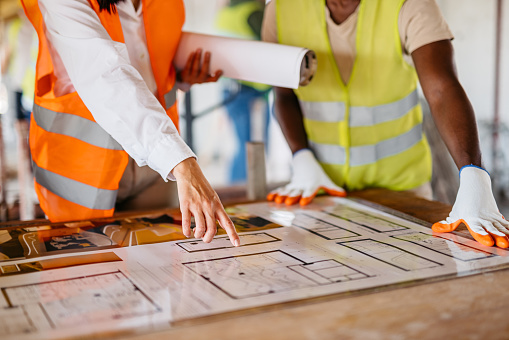 Female architect showing the construction plan to the construction worker working on a construction site (building interior). Close-up.