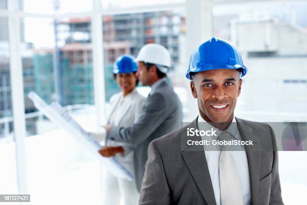 Male Engineer With Colleagues In The Background Stock Photo - Download Image Now - African Ethnicity, Engineer, Adult