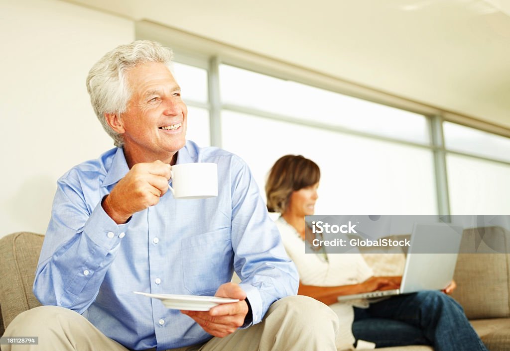Dojrzały człowiek pije kawę i kobieta za pomocą laptopa - Zbiór zdjęć royalty-free (50-59 lat)