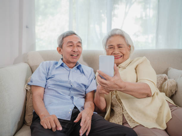 istock Asian senior couple enjoy using smart phone while sitting on sofa in living room 1811299876