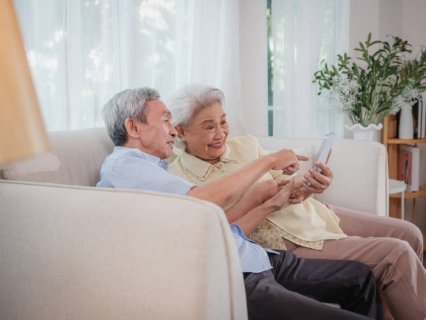 istock Asian senior couple enjoy using smart phone while sitting on sofa in living room 1811311241