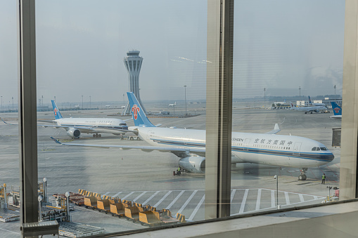 Airport hall with armchairs and luggage carts and blue plane seen outside