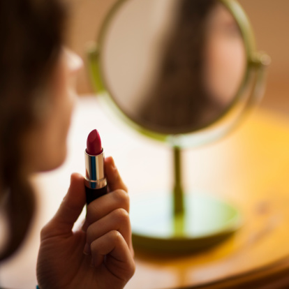 A woman looking into a mirror getting ready to apply her lipstick...