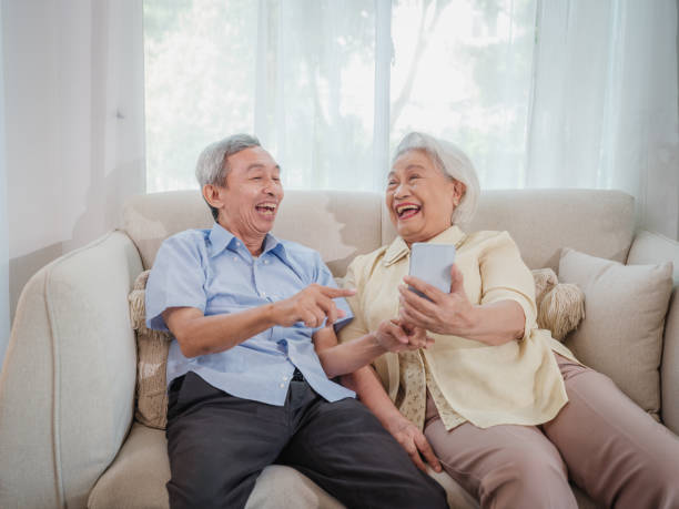 istock Asian senior couple enjoy using smart phone while sitting on sofa in living room 1811323213