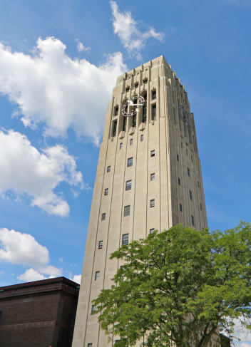 The Burton Bell Tower on the University of Michigan's Ann Arbor campus is a central fixture and landmark in the campus landscape. There is a bright reflection coming off of the face of the clock helping to center attention on it.