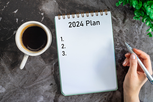 Woman is writing 2024 goals for new year resolutions plan.