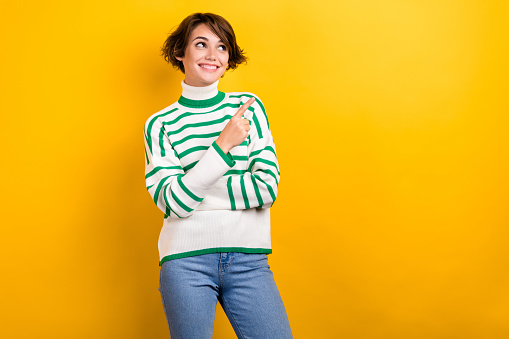 Photo of attractive young woman look direct empty copy space poster wear oversize sweater jeans isolated yellow color background.