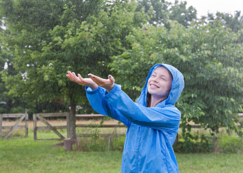 Confident smiling young girl enjoying a pouring rainfall in the backyard