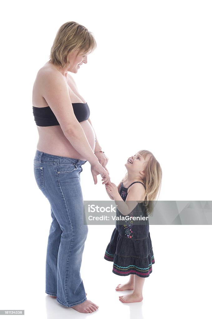 Four year old smiling up at pregnant mom. Vertical studio shot on white of pregnant woman holding hands with 4 year old daughter. 2-3 Years Stock Photo