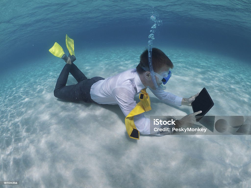 Traveling Businessman Relaxing Using Digital Tablet Underwater Traveling businessman using digital tablet relaxing on the floor of a clear tropical ocean Business Stock Photo