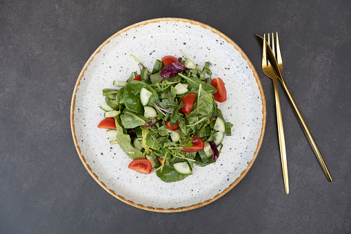 High angle view of a colorful spring salad on rustic white wood table. Included ingredients: Olive oil, peppermint, chia, tomatoes, broccoli, lettuce, bell peppers, mushroom, carrots, radicchio and almonds.