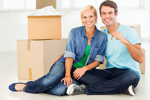 istock Couple With House Keys Sitting Against Stacked Cardboard Boxes 181135572