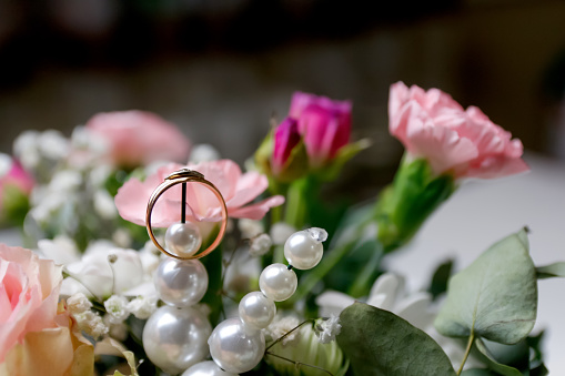 A single golden wedding ring surrounded by pink flowers, creating a romantic scene on a white background. Copy space. Out of focus.