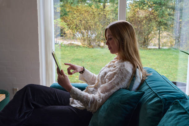 istock Young woman sitting in teal sofa holding a digital tablet 1811361274