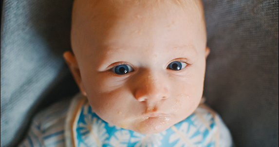 In a candid high angle close-up,a baby boy's endearing portrait reveals the aftermath of a playful meal,with a messy mouth,while seated on a bouncer at home