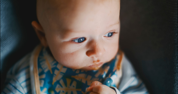 In a close-up moment of contemplation,a baby boy with a messy mouth gazes thoughtfully away while resting on a bouncer at home. The image captures the innocence and introspection
