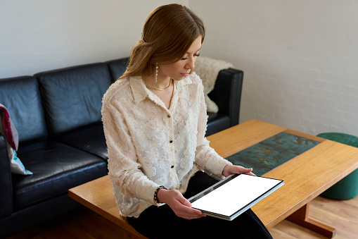 View over shoulder. Young woman sitting on table using digital tablet. Camera looking at screen having a clipping path for easy change of content