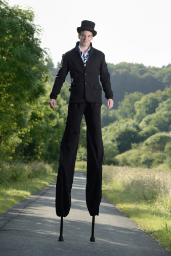 Young artist walking on stilts. With a black suit. Taken in morning time with backlit.