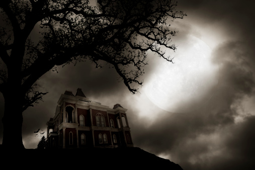 A haunted house on a hill in front of a full moon.