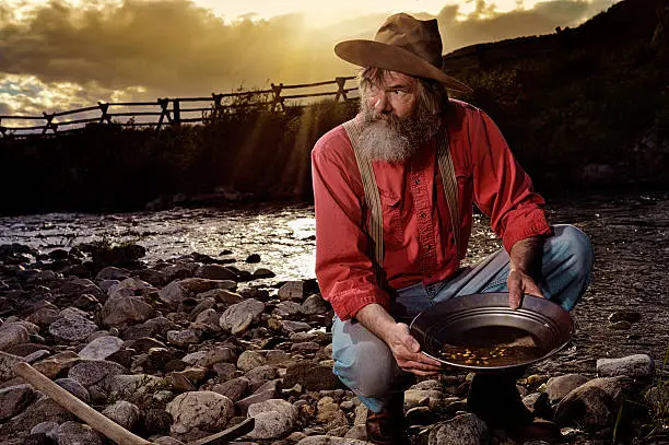 "Old Prospector Panning for gold.  Liquid gold from the sun pouring in over his shoulder from a hot western sunset.  You can see the gold nuggets in his pan.  Striking it Rich!!  Old hat, suspenders, red shirt.  Miners pan, pick ax, and a prospector's dream of a stream to work from."