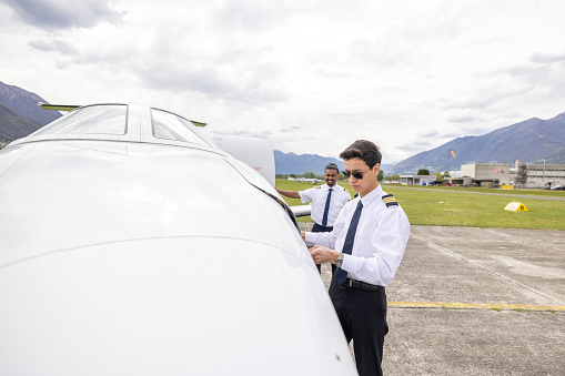 Males pilots preparing private jet for flight, one stores bags away