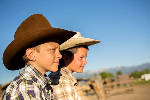 Young cowhands at the corral, watching horses.    