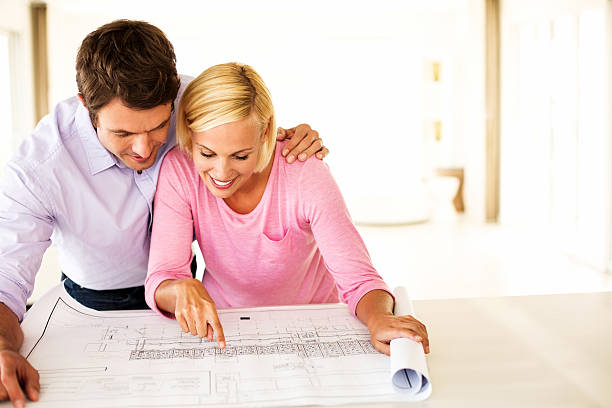 Couple Discussing Over Blueprint At Table In House