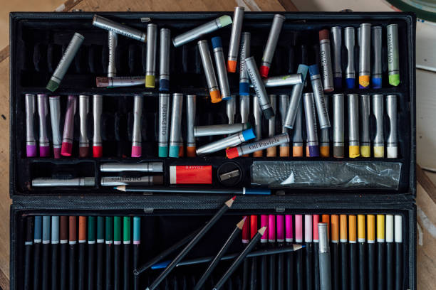 Directly above close up of a selection of multi coloured oil pastels in a box with a set of multi coloured pencils, a ruler, pencil sharpener and eraser.