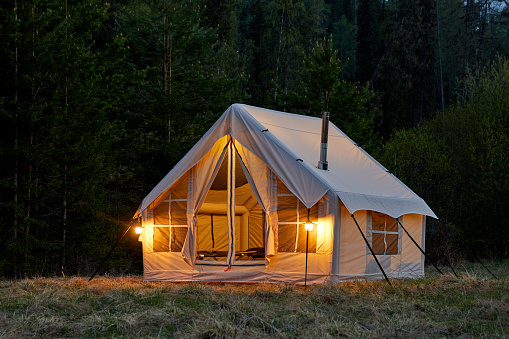 Large camping tent in a natural setting at sunset. Warm cozy light inside a camping tent.
