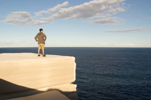 A man stands atop a rock cliff nicknamed the Cheese Block, due to its pale yellow colour and shape. Royal National Park, NSW, Australia.