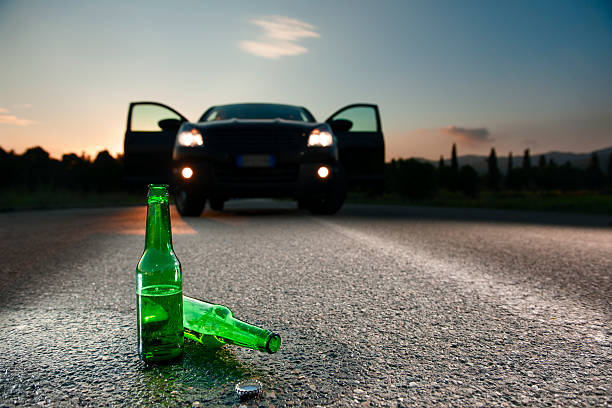 The Dangers Of Alcohol.Color Image Two bottles of beer have fallen in the street in front of a car stopped, with the doors open and the lights on. pics of drunk driving accidents stock pictures, royalty-free photos & images