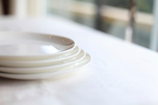 Four white plates stacking together on a white cloth dining table.
