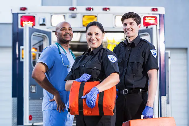 Paramedics and doctor standing at rear of ambulance.  Focus on paramedics (30s, Hispanic).