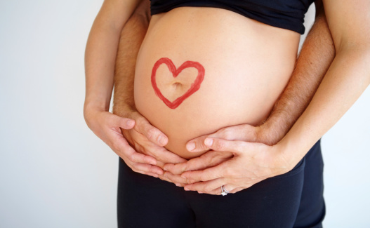 Pregnant woman's belly with her partner's hands wrapped around her and a heart shape painted on it