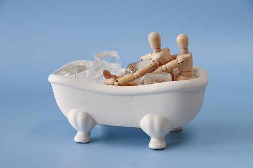 Stock photo showing close-up view of ice cubes in a model, Victorian style, white ceramic freestanding curved roll top bath with claw feet.  Ice baths are often used in spas and health retreats is a therapeutic treatment or by professional and amateur athletes after workouts to ease sore muscles. Health and therapy concept.