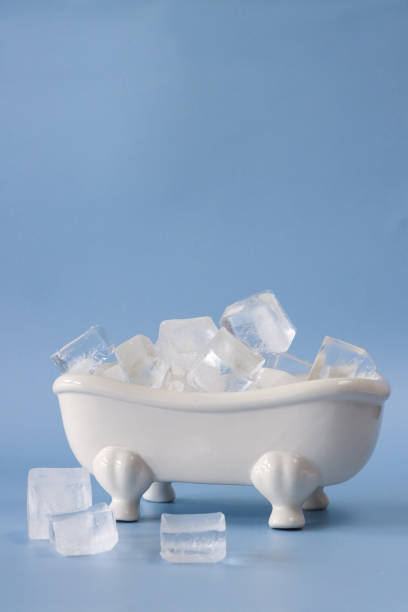 Close-up image of model, Victorian style, white ceramic freestanding curved roll top bath with claw feet filled with cubes of ice, light blue background, health and therapy concept, copy space stock photo