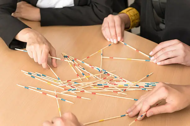 Hands of four business people on the table playing with mikado, pick-up sticks.