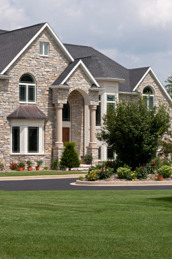 The front of a large stone mansion with tall columns and beautiful landscaping.