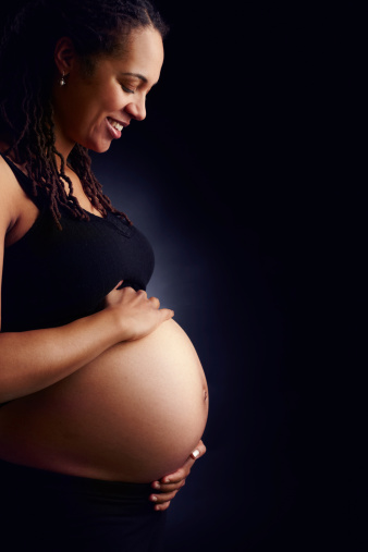 A side profile of a tranquil pregnant woman holding her bare belly and looking down