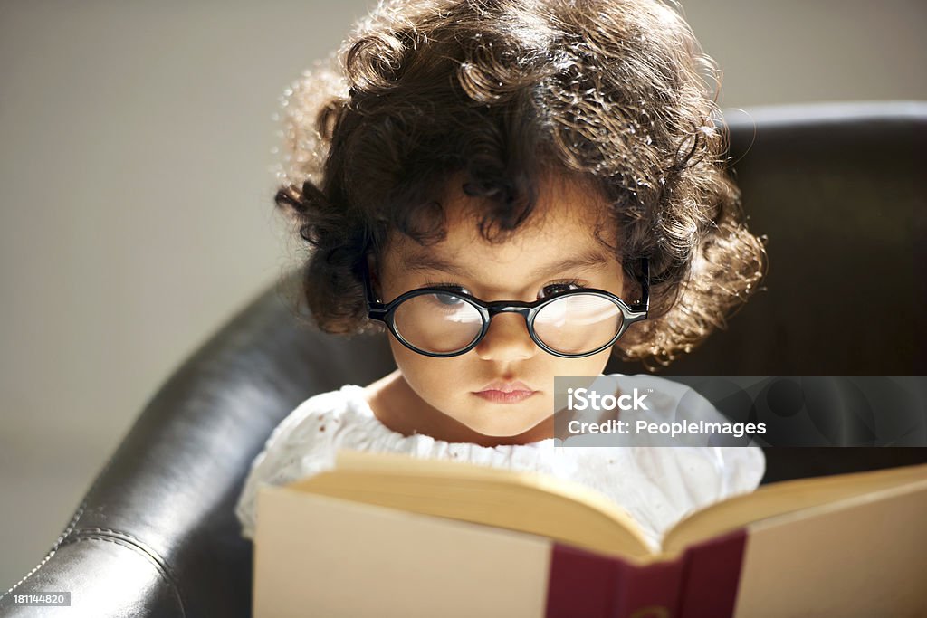 Intelligent little bookworm A cute little girl wearing glasses and reading a book Child Stock Photo