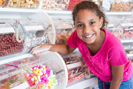 Smiling nine years old afro caribbean girl shopping for candies in a candy store