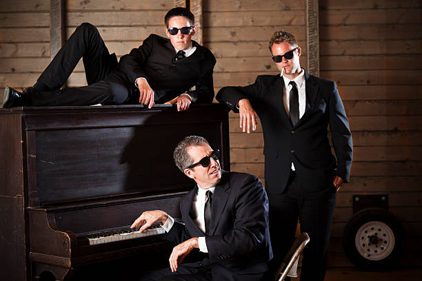 istock Music:  Three men, black suits wearing sunglasses at piano.  Smoking. 181146049