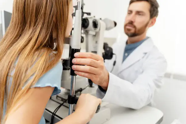 Ophthalmologist examining little girl eyes with modern equipment in optics. Health care concept
