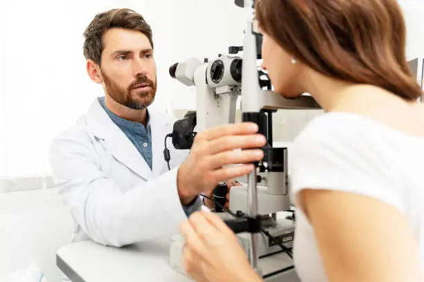 Male optometrist using a binocular slit-lamp while examining the eye of female patient. Medical examination