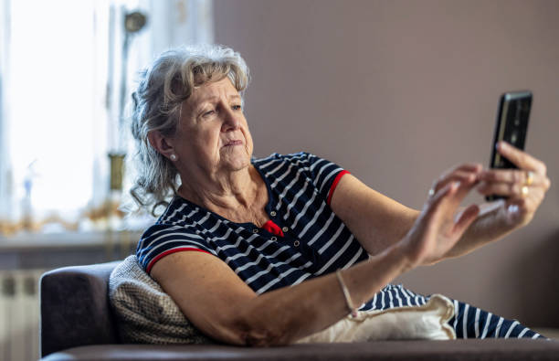 istock Elderly woman sitting on couch and using mobile phone at home 1811476621