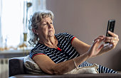 Elderly woman sitting on couch and using mobile phone at home