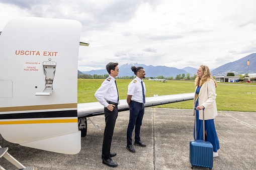 Pilots greeting businesswoman on the tarmac in front of a private jet plane.
People travel luxury private concept