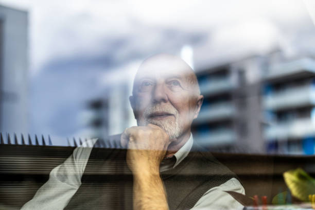 istock Portrait of thoughtful senior man looking through window 1811478654
