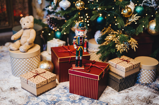 Nutcracker soldier stands guard among wrapped Christmas gifts and a teddy bear with a festive tree in the background