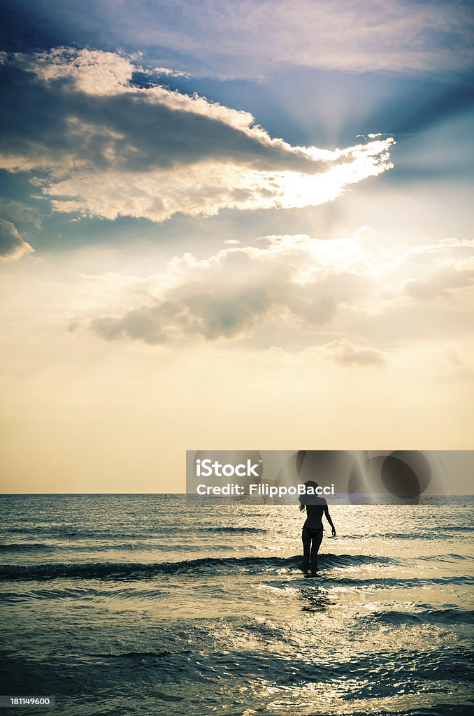 Jeune femme marchant dans la mer sur coucher de soleil - Photo de 25-29 ans libre de droits